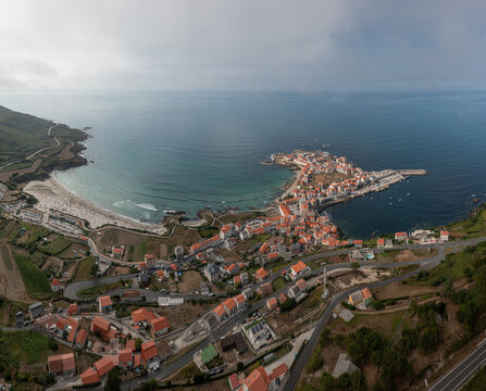 Aerial view of the coastal village of Caion, featuring red-tiled rooftops, a sandy beach, and a small harbor along the Atlantic coastline in Caion, A Coruna, Spain.