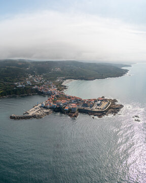 Aerial view of the coastal town of Caion, featuring its harbor, stone buildings with orange rooftops, and the surrounding Atlantic coastline, Caion, A Coruna, Spain.