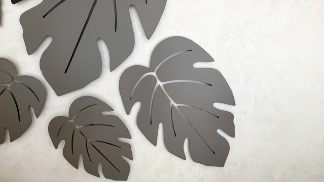 Modern decorative monstera leaf wall art in neutral gray tones on a textured light background, minimalist botanical interior decor with abstract tropical leaf shapes.