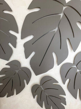 Modern decorative monstera leaf wall art in neutral gray tones on a textured light background, minimalist botanical interior decor with abstract tropical leaf shapes.
