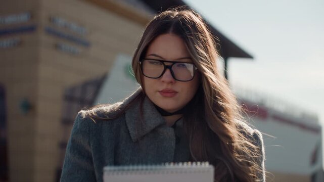 Architectural planning outdoors visually captured. Beautifully lit outdoor scene of woman drawing plans thoughtfully. Sunshine bathes woman working on architectural designs with notepad nearby