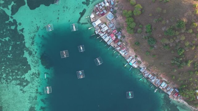 Aerial view of Pulau Kukusan coastal village with fish farming cages in turquoise waters in Komodo, East Nusa Tenggara, Indonesia.