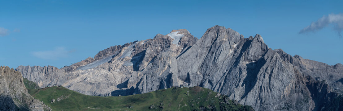 View of Piz Boe mountain peak with rocky slopes, glacier remnants, and green alpine meadows under a clear blue sky in Canazei, Trentino-Alto Adige, Italy.