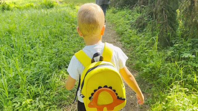 A young boy wearing a yellow backpack walks on a sunny park path. He feels happy and peaceful during a joyful outdoor adventure.