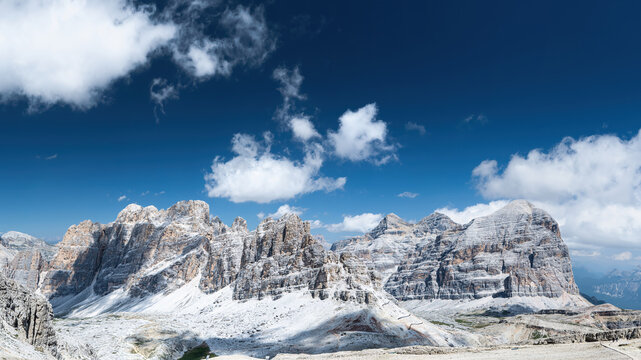 View of the rugged limestone peaks of Cima Tofana di Mezzo under a deep blue sky with scattered white clouds and dramatic rocky slopes in Cortina d'Ampezzo, Veneto, Italy.