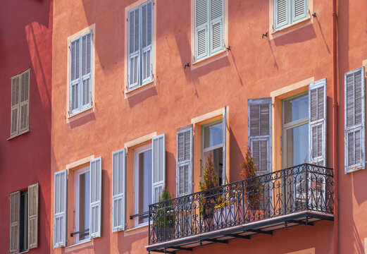 View of the colorful facade of a historic building in Nice Old Town with traditional wooden shutters and a wrought iron balcony in Nice, Provence-Alpes-Cote d'Azur, France.
