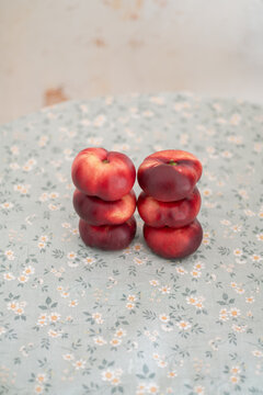 Red flat nectarines arranged in balanced vertical stacks against a softly blurred neutral wall.