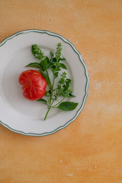 Fresh tomato with green basil leaves and white blossoms on the plate