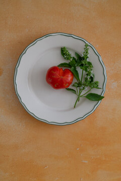 Ripe red tomato and flowering basil on a white plate