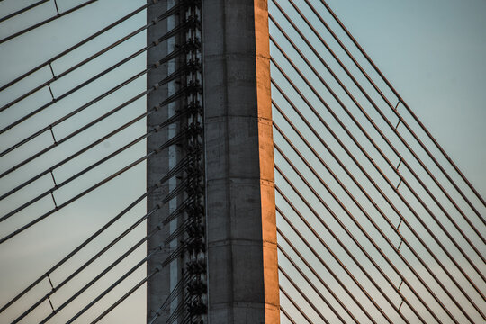 View of the concrete pylon and steel cables of a cable-stayed bridge illuminated by golden hour light in Riga, Latvia.