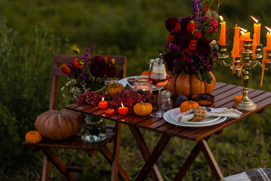 Cozy autumn table decoration for a thanksgiving party outdoors. Grapes, fig, rose wine, candles, pumpkins as decor. Elegant wedding fall arrangement, beautiful setting for a romantic proposal