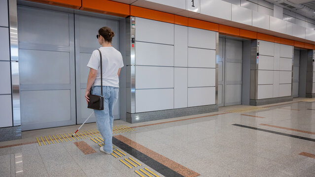 A blind woman waits for a train on the subway.