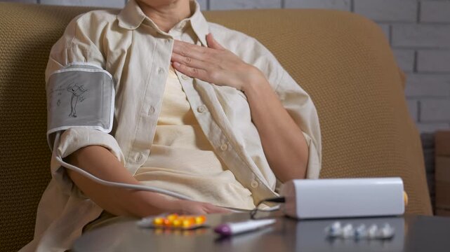 Woman measuring blood pressure having heart pain. Unhealthy senior woman measuring her blood pressure with an electronic tonometer at home, feeling unwell and experiencing chest pain while