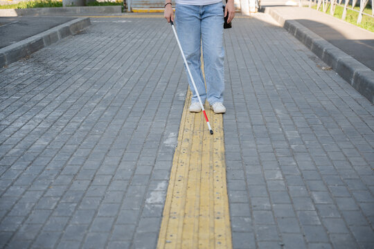 A blind woman walks using a cane and tactile tiles.
