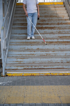 A blind woman descends a staircase. Close-up of her feet and a tactile stick.