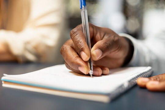 Bookkeeper in the office writes financial figures on paper, transcribing information with a pen and crosschecking data from reports and a notepad during late-night accounting work.