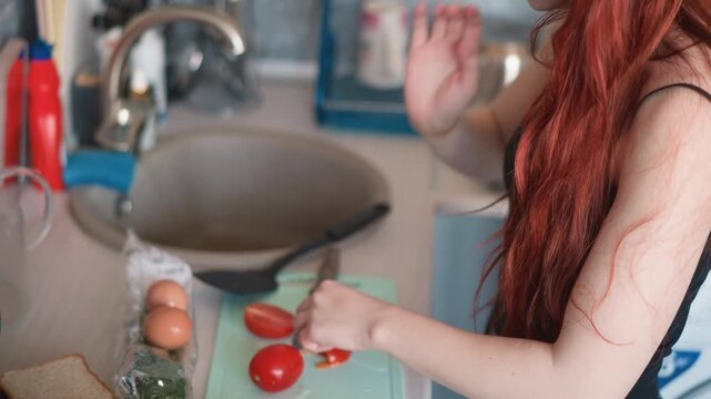 Pan frying toast on stove with hands chopping tomato nearby, redhead woman preparing morning meal at counter, eggs and bread staged on board, sizzling skillet and utensils in motion, bright kitchen