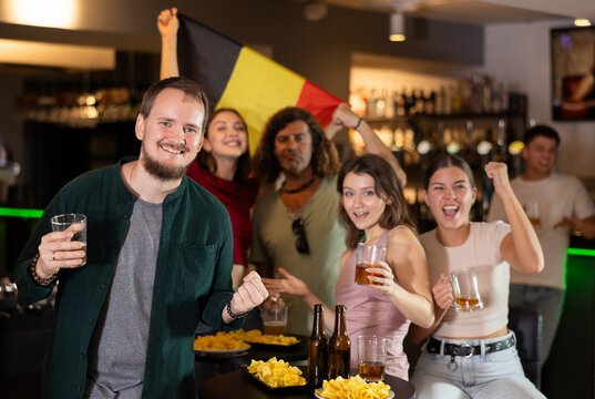 Happy girls adm men with Belgian flag celebrates the victory of her favorite team in a beer bar