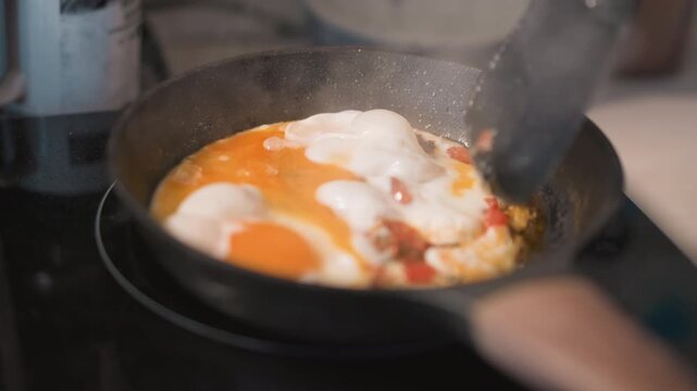 Rapidly frying eggs with sizzling sounds. Cooking eggs quickly while stirring in hot skillet. Efficiently preparing breakfast eggs through swift spatula movements and sizzling sounds