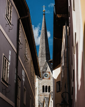 View of the spire of the Evangelical Church of Hallstatt framed by historic buildings in a narrow alleyway in Hallstatt, Upper Austria, Austria.