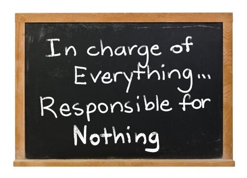 In charge of everything, responsible for nothing, written in white chalk on a black chalkboard isolated in a wooden frame on white