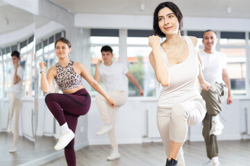 Fototapeta premium Sporty smiling young brunette practicing rhythmic aerobics during group workout in fitness studio. Active lifestyle concept