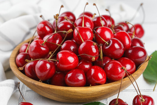 Fresh ripe red sweet cherries in wooden bowl with green leaves on light textured background. Healthy organic summer fruit, juicy red berries, natural freshness, healthy eating, seasonal food