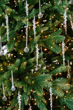 Christmas tree branch decorated with clear glass ornaments, glass icicle decorations and warm glowing lights, elegant festive background with winter atmosphere. Holiday mood, aesthetic decor