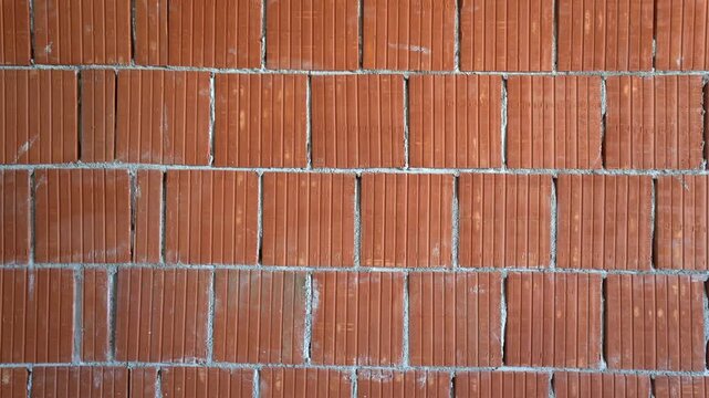 Texture and pattern of a red hollow clay brick wall in progress on building site.