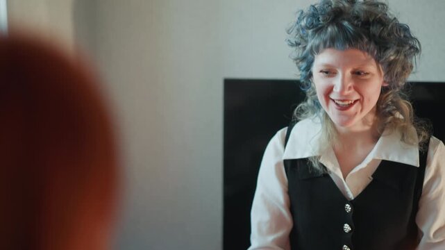 Caucasian woman fortune teller smiling during consultation, curly gray hair and candlelight create warm intimate room, spiritual advisor offers gentle prediction and guidance to redheaded client,