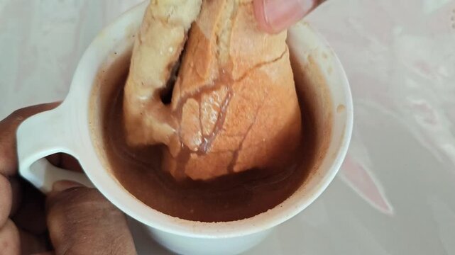Dipping Crusty Bread Roll into Hot Pinole Beverage Cup