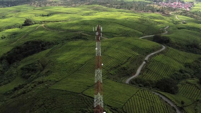 Aerial view of a telecommunications tower standing amidst the lush green tea plantations of Kayu Aro in Kab. Kerinci, Jambi, Indonesia.