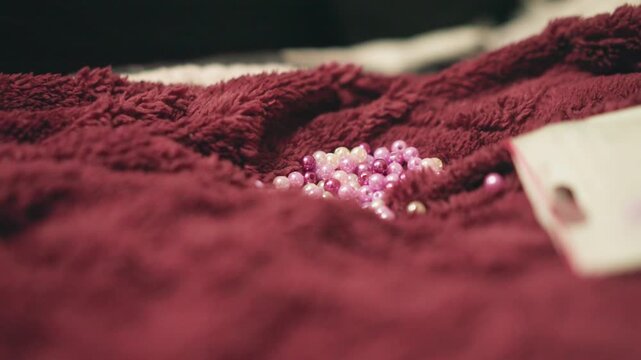 Pink beads on burgundy towel styled for product flatlay, visible tag and soft pile, ecommerce friendly closeup with shallow focus, trendy lifestyle composition ideal for catalog and social marketing.