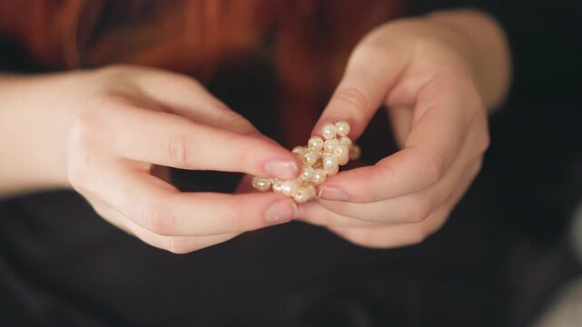 Closeup hands holding pearl beads, fortune teller gently counts and turns heirloom jewelry soft warm lighting and shallow depth of field create intimate contemplative mood, delicate fingers, subtle