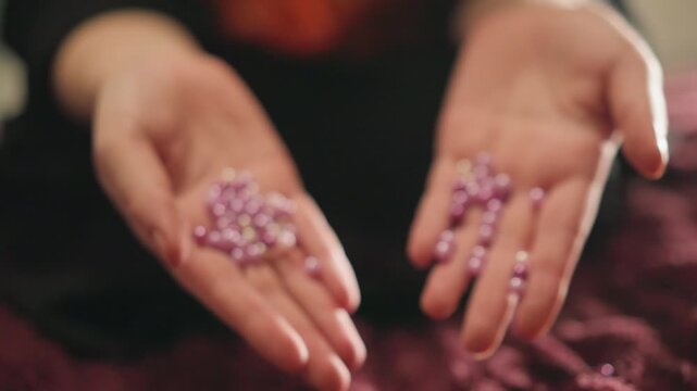 Open caucasian hands releasing purple pearls onto velvet, slowmotion spill, somber toned gesture of surrender, symbolic release and closure, cinematic bokeh, mysticcore undertone, emotional foresight