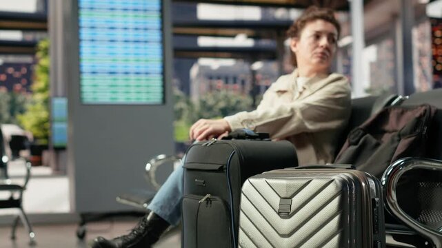 Woman stands alone beside heavy baggage in a bus station during a delay, looking uncertain and concerned while surrounded by bags before a difficult departure.