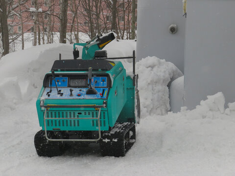 View of a teal snowblower clearing deep snow in Niseko, Hokkaido, Japan.