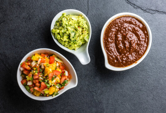 Traditional famous mexican sauces chocolate chili mole poblano, avocado guacamole and salsa pico del gallo on slate gray background