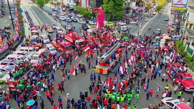 Samarinda, East Kalimantan, Indonesia - 17 August 2026: Aerial view of a festive Independence Day parade featuring fire trucks and crowds of people waving Indonesian flags.