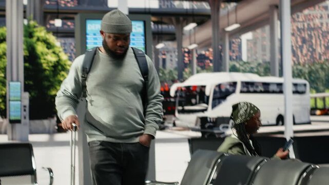 Passenger carrying baggage checks bus connections on a departure board, reading the electronic timetable in the waiting area before the next shuttle route.