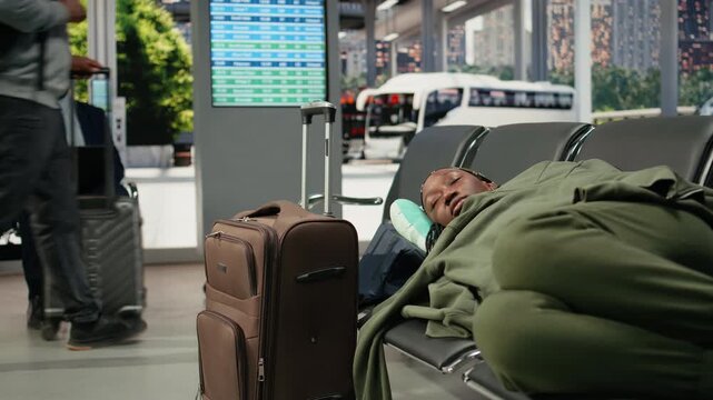 Tired woman rests on bus terminal seats during a long wait before a cancelled departure resumes, sleeping on baggage during the delayed coach journey.
