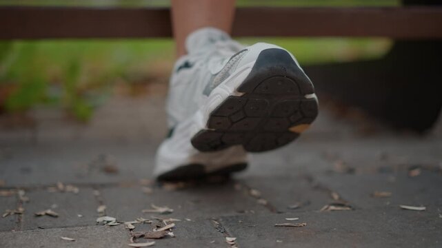 Low angle close view of right athletic sneaker mid step with heel raised and forefoot pushing off rectangular paving stones, showing weight transfer, toe roll, and brisk outdoor motion in park light