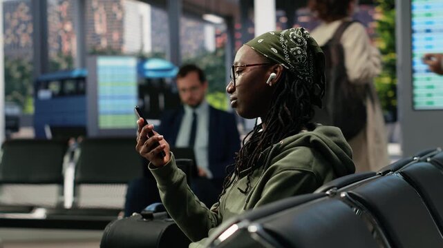 Woman sends an audio message on her phone in a bus terminal while waiting, wearing earphones and speaking into the smartphone before departure.