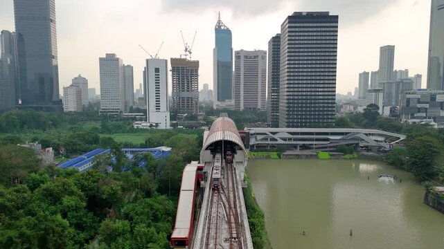Jakarta, Indonesia - 19 July 2026: Aerial view of the MRT station tracks surrounded by modern skyscrapers, lush greenery, and a river in the city center.