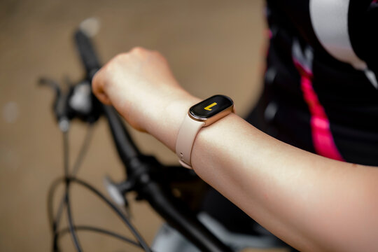 Cyclist woman checking fitness tracker watch on wrist riding mountain bike outdoors. Sports technology and active lifestyle tracking concept.