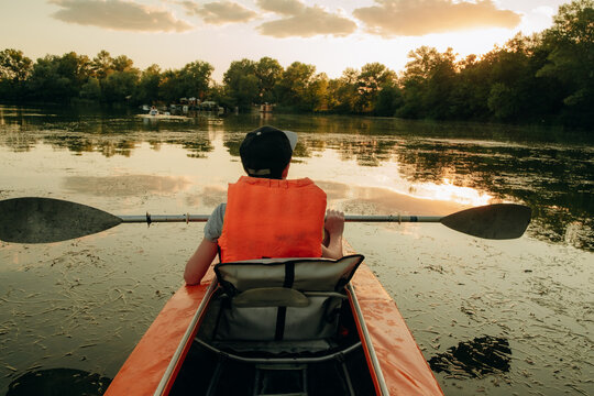 Boy in life jacket kayaking on calm river water during sunny summer day, outdoor active lifestyle and water sport concept
