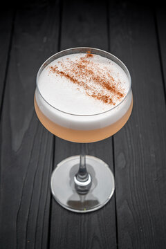 Drink in a glass on dark table. A cocktail with foam and a sprinkle of spice sits in a glass on a wooden table, ready to be enjoyed.