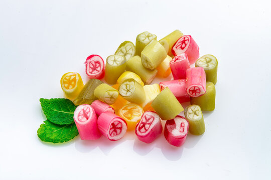 Assorted colorful hard candies with mint leaves on white background. Heap of bright fruit caramel drops with green herbal sprig in studio.
