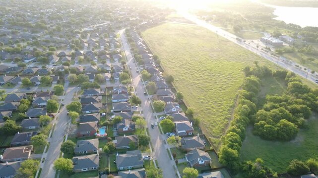 Golden sunbeams illuminate pastures bordering Lakewood Estates near Eldorado Parkway. Linear roadway corridors, rooftop clusters, distant lake waters showcase suburban growth, Little Elm, Texas