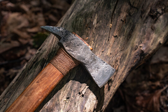 Handmade forged steel axe on ancient wooden log in forest close up.
